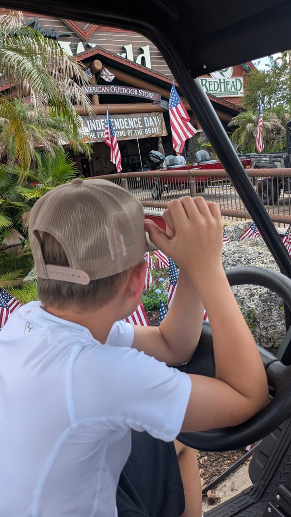 Jayden seen from behind at the wheel, looking at boats and flags outside Bass Pro Shops