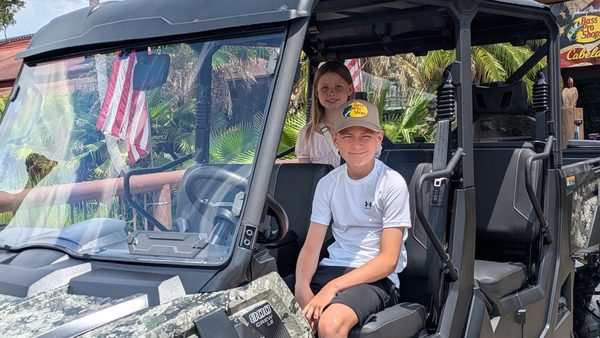 Jayden in a Bass Pro Shops cap at the wheel of a side-by-side, Olivia in the back seat